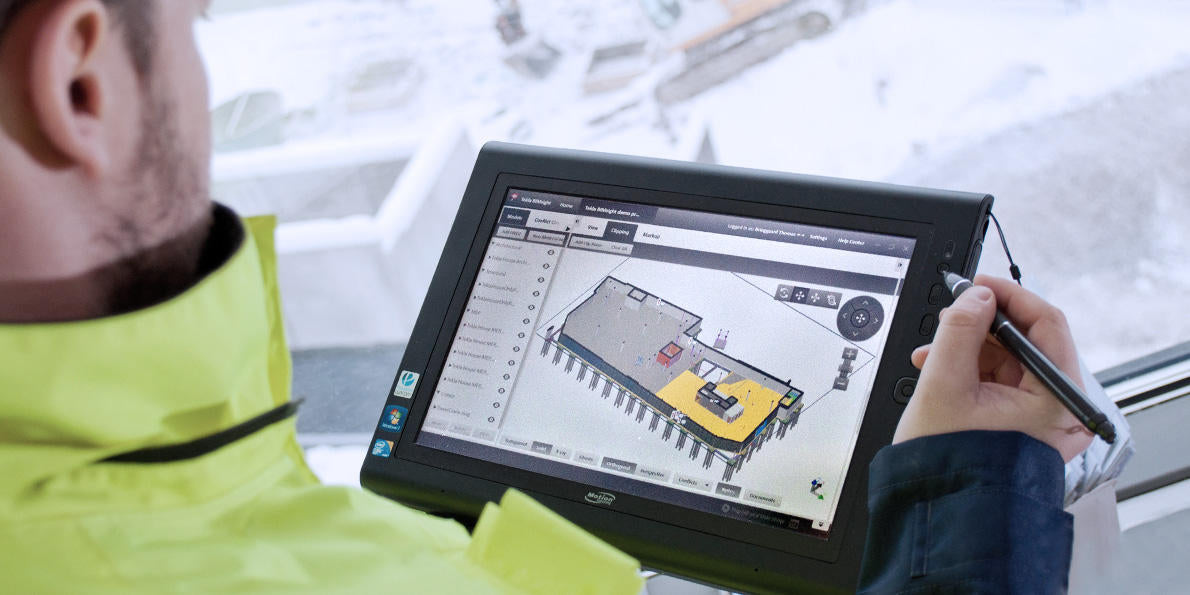 Engineer using a tablet to manage digital construction plans in a snowy site environment.